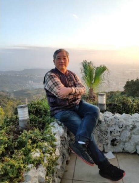 照片為張曉生副校長坐在矮牆上，背景為遠方的山